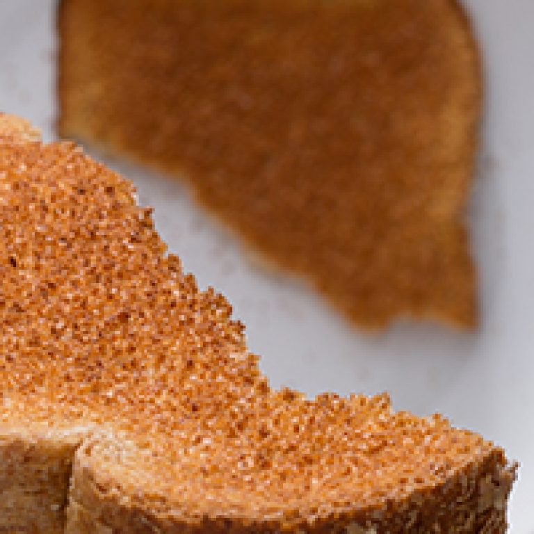 Close up of a man's hand holding toast over plate from a unique point of view. Shallow depth of field with focus on toast in hand.