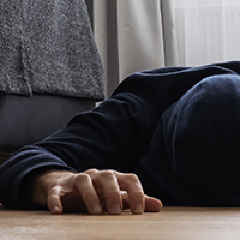 Young man in dark hoodie lays on a floor at home, emotional crisis concept
